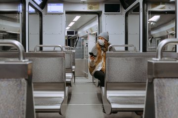Woman sitting in an empty subway/train car wearing a mask